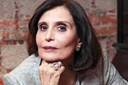 Retrato de una mujer de tez clara y cabello oscuro liso, con una mirada seria y pensativa. Viste una chaqueta clara de un tejido texturizado y lleva un anillo grande en el dedo anular de su mano derecha, que descansa en su barbilla.