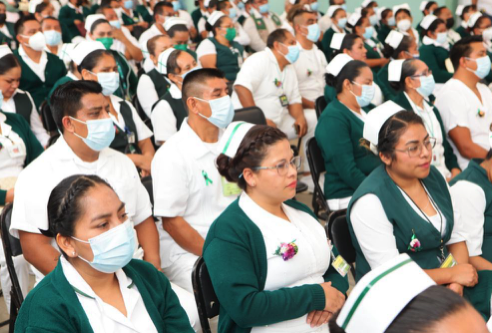 Vista parcial de un numeroso grupo de profesionales de la salud, la mayoría mujeres, sentados y escuchando atentamente durante un evento o conferencia. La mayoría viste uniformes de enfermería en tonos verde oscuro y blanco, con cubrebocas azul claro.