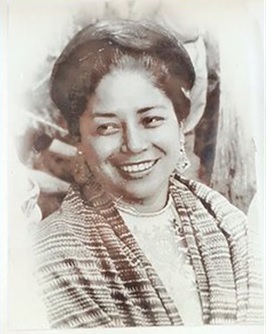 Se muestra una fotografia en blanco y negro de una mujer sonriendo, ella es Adoración Youshimatz Morales. Pionera feminista quien impulso el acceso a la educación, formadora de parteras y promotora de derechos.Su legado vive en cada mujer que transforma su comunidad con dignidad y justicia social.