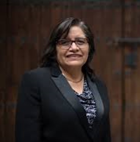  La imagen  es un retrato de Lilia Meza Montes, quien se muestra en un exterior, vestida de manera formal, con un traje negro y sonriendo a la cámara. Es la primera Es la primera poblana en obtener un doctorado en Física en la BUAP.Con más de 100 trabajos presentados y múltiples premios, sigue abonando por la igualdad de género y la inclusión de mujeres en ciencias exactas y tecnológicas. Su labor en la Red Mexicana de Ciencia, Tecnología y Género del Conacyt es clave para derribar barreras en el ámbito científico.