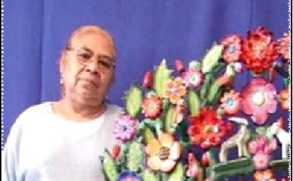  En la imagen se muetra a una mujer posando junto a un arreglo de flores de diferentes colores y tamaños. Ella es Isabel Castillo Orta, quien fue una destacada artesana con más de 60 años de trayectoria en la técnica del barro policromado, quien compartió su conocimiento con jpovenes artesanos y promovió la igualdad de género en su comunidad.