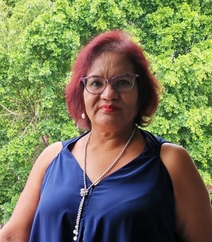 La imagen es un retrato de Alejandra Valdivia Márquez, una mujer de piel clara con cabello rojizo oscuro y corto, a la altura de los hombros. Su rostro muestra una expresión serena y amable, con una ligera sonrisa. El fondo de la imagen  verde borroso, sugiriendo un espacio exterior. Ella es Tanatóloga, feminista, activista por la igualdad de género y sobreviviente al cáncer.Su propia experiencia la ha convertido en un ejemplo de resiliencia y empoderamiento, inspirando a otras mujeres a salir adelante con fortaleza y esperanza.